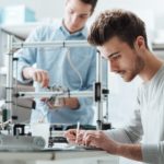 Man works on 3D printer while another works on a tablet