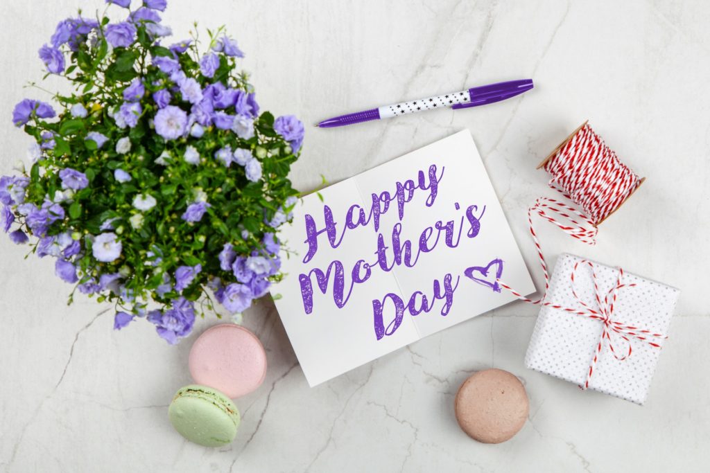 "Happy Mother's Day" written on a card, with flowers, a present, and macaroons around it