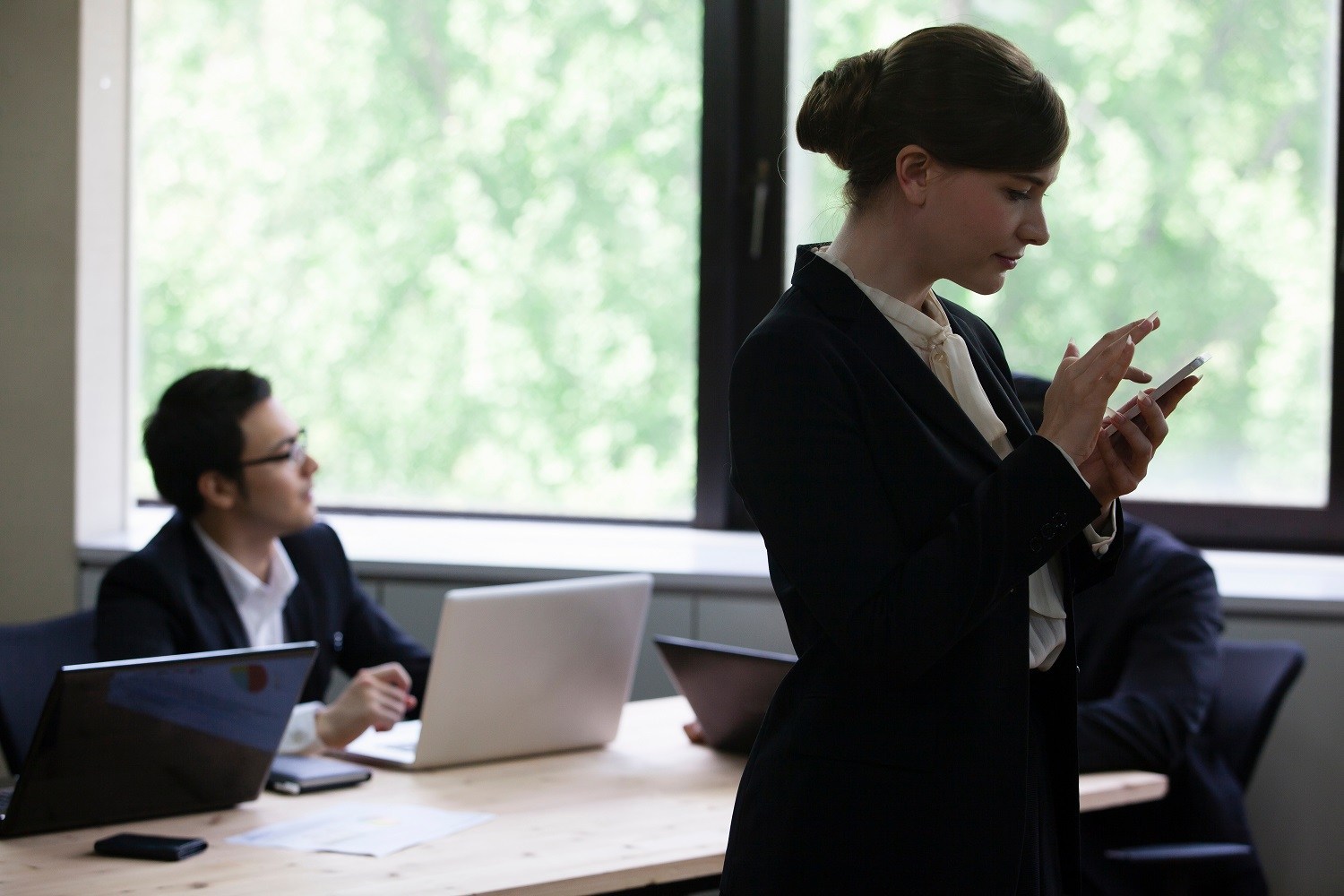 A woman using her phone at work with a man looking away in the background