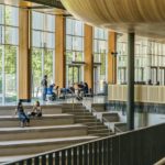 students sitting on stairs with large glass windows behind them