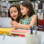 two children looking at an iPad in a library