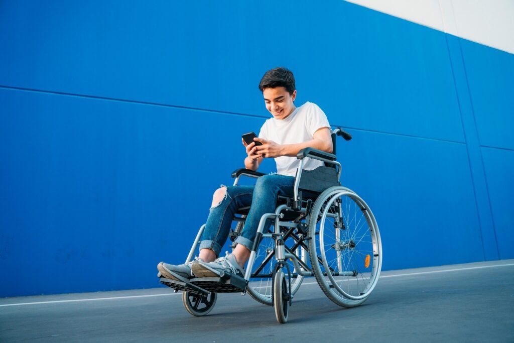 Youth seated in wheelchair, outdoors, using his phone and smiling