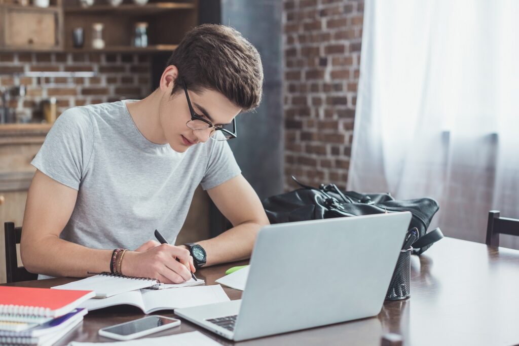 a student writing notes, with a laptop in front of him