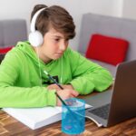 a child using a laptop, wearing headphones