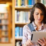 Student standing in a library, using a tablet