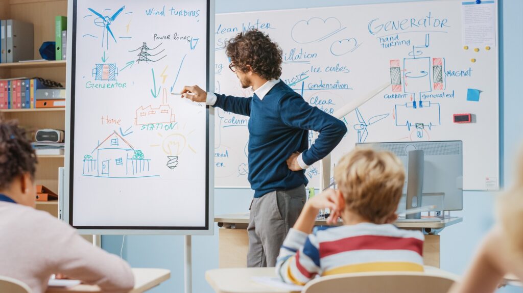 A teacher sketching a process for wind energy generation, with a group of students seated and watching