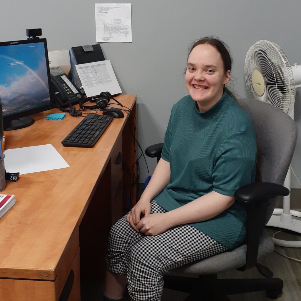 Rayanne seated at her desk at work. She is smiling