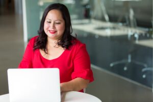 Woman wearing red, seated at a desk, typing on a laptop