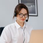 Woman seated at a desk, using headphones while looking at a laptop