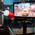 A LipSync is mounted in front of a TV which is a displaying a racing video game