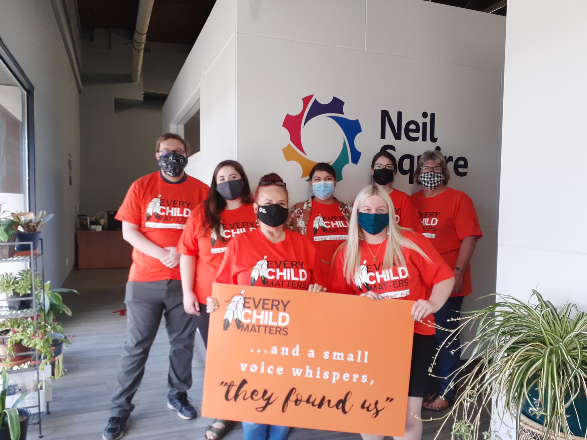 Neil Squire Regina staff wearing orange "Every Child Matters" shirts and black masks holding an orange sign, saying, "Every Child Matters ...and a small voice whispers, 'They found us.'"