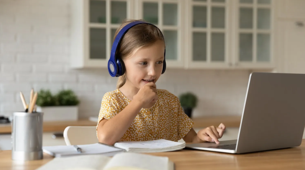 A child using headphones, looking at a laptop, seated at a table