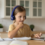 A child using headphones, looking at a laptop, seated at a table