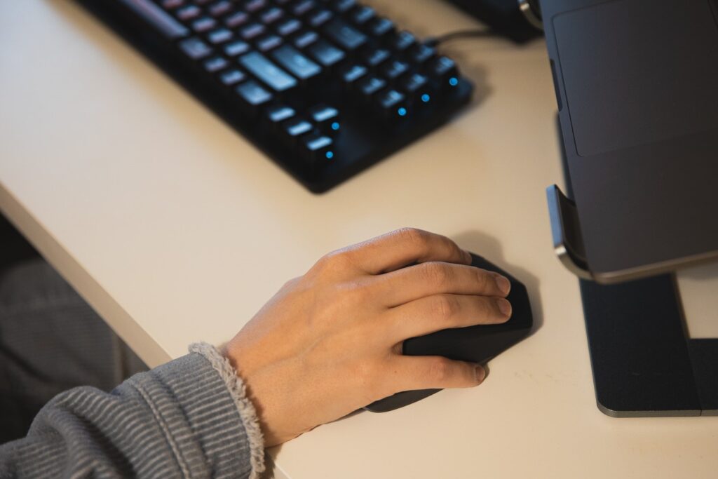 a person's hand using a computer mouse, with an external keyboard visible in the background