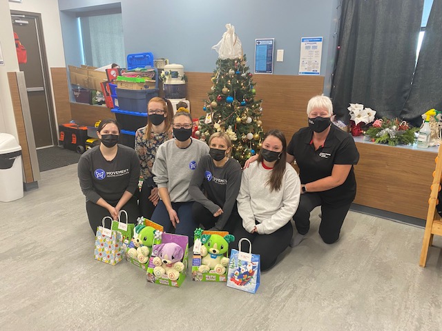 Makers Making Change Central Region coordinator Suzanne Winterflood poses with the Movement Centre of Manitoba staff in front of a Christmas tree and with the toys in front.