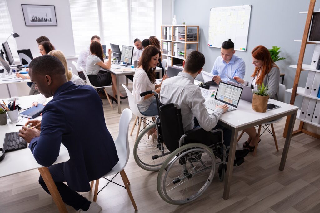 diverse groups of people working in an office, including a man in a wheelchair