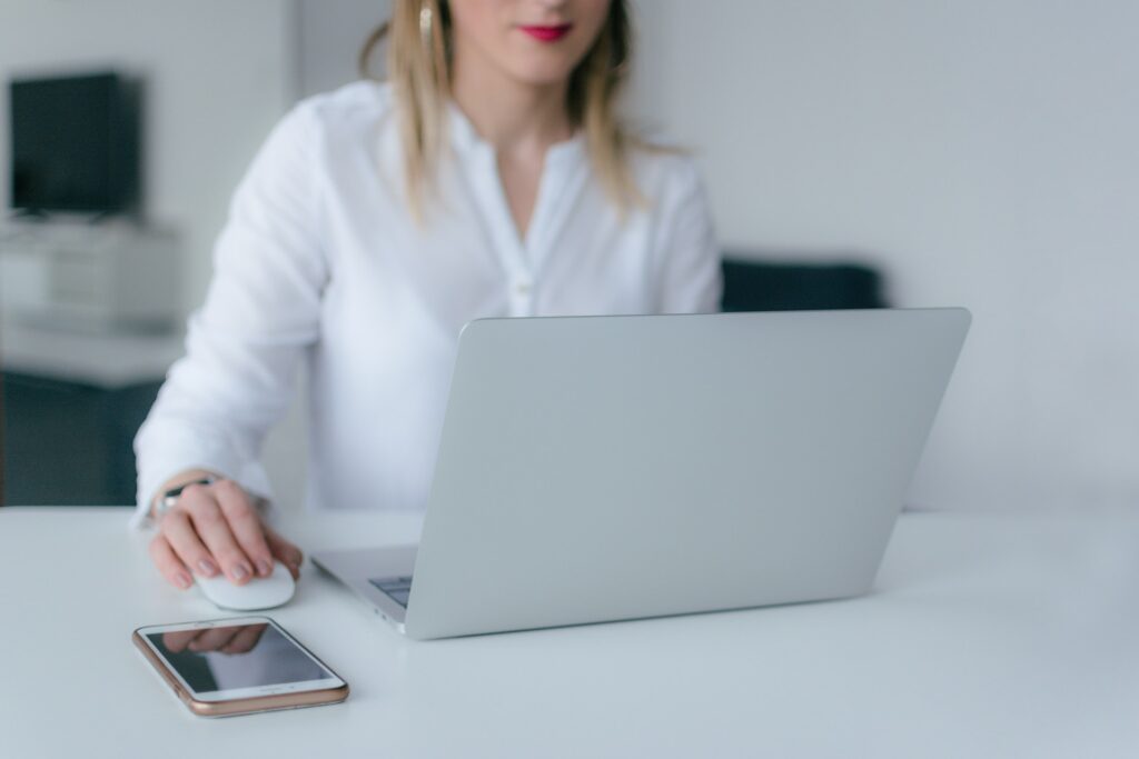 a woman uses her laptop, with her phone nearby on the table