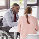 a woman works with a man in a wheelchair on a laptop