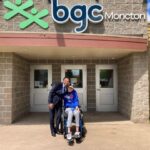 Adam in a wheelchair with BGC Moncton Executive Director Moncef Lakouas outside the BGC Moncton building