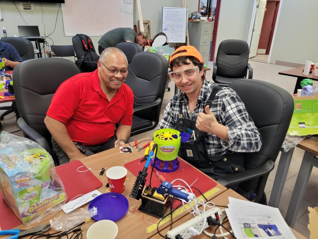 Neil Squire employee Dale and a volunteer flash a thumbs up as they are working on adapting a toy