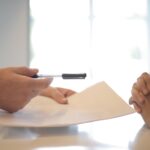 a person in a suit handing a customer a paper and pen to sign a document