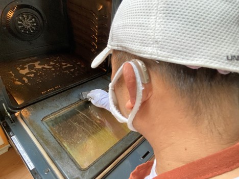 Eliezar cleaning the inside of an oven, while wearing his new hearing aids