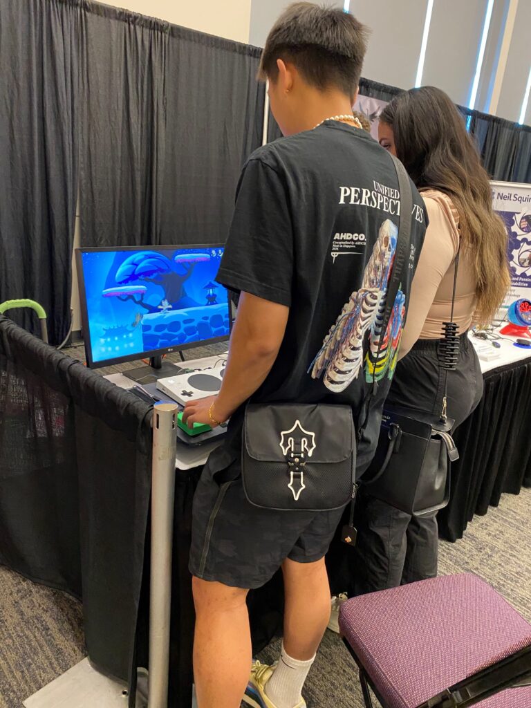 Two people standing playing the Adaptive Gaming set-up at the Makers Making Change booth