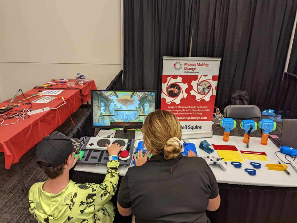 Makers Making Change regional coordinator Shanelle demonstrating the Adaptive Gaming set-up to a video game player at the Edmonton Maker Faire