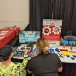 Makers Making Change regional coordinator Shanelle demonstrating the Adaptive Gaming set-up to a video game player at the Edmonton Maker Faire