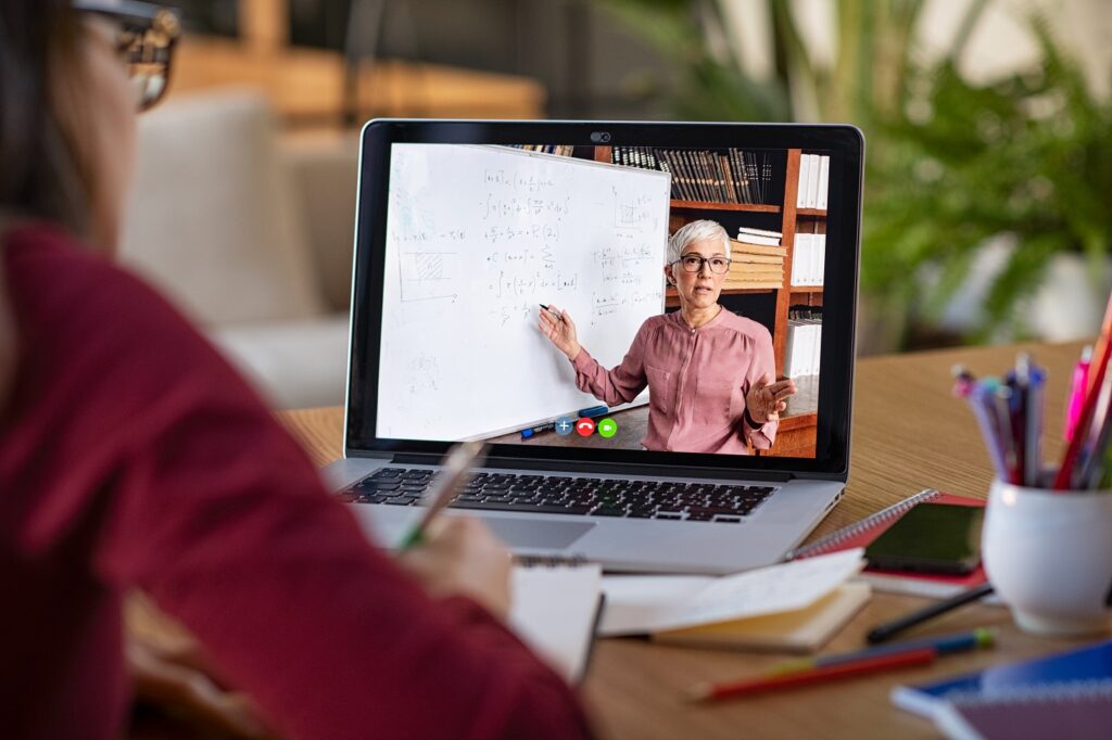 a person watching a lesson her laptop, featuring a lecturer demonstrating mathematical equations on a whiteboard