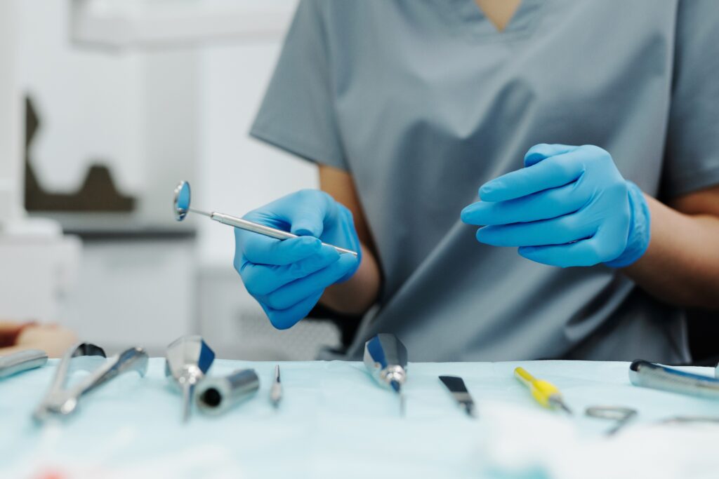 a person wearing gloves and dental scrubs grabs some dental tools