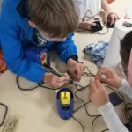 kids making devices together, with one kid holding a soldering gun