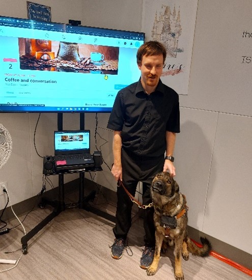 Blaine and his guide dog Oscar in front of TV screen showing his Facebook event that he created