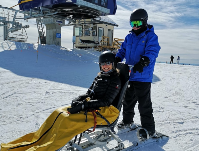 Sonja on a snowy mountain in an adapted ski set-up, with a person pushing her