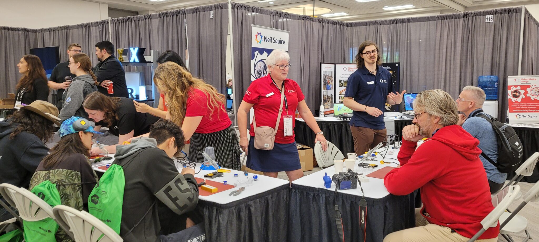 The Makers Making Change team work the booth as students work on devices and teachers supervise.