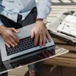 A man using a laptop while sitting on a bench.