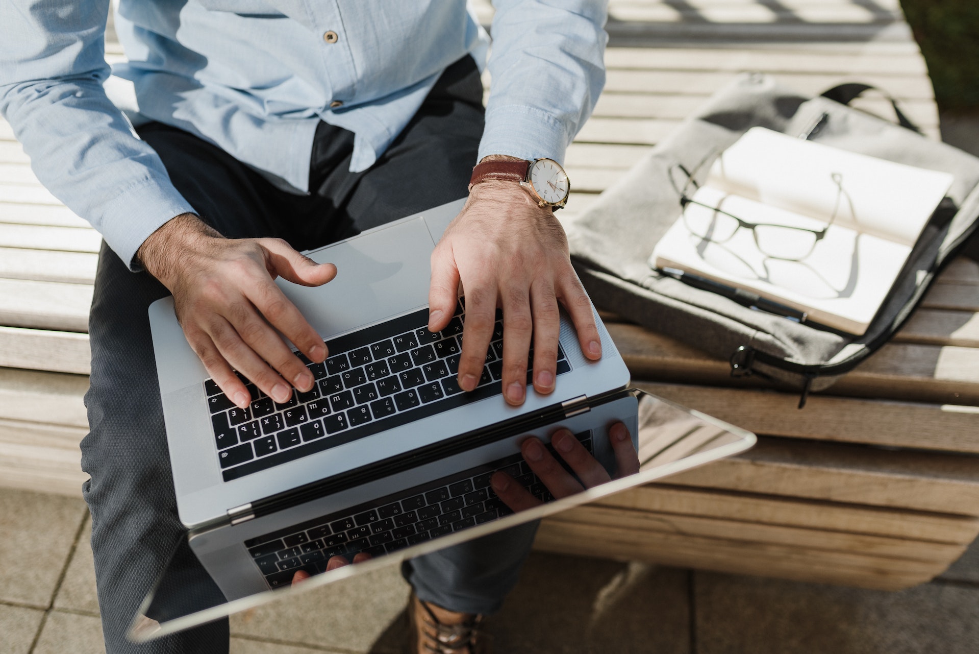 A man using a laptop while sitting on a bench.