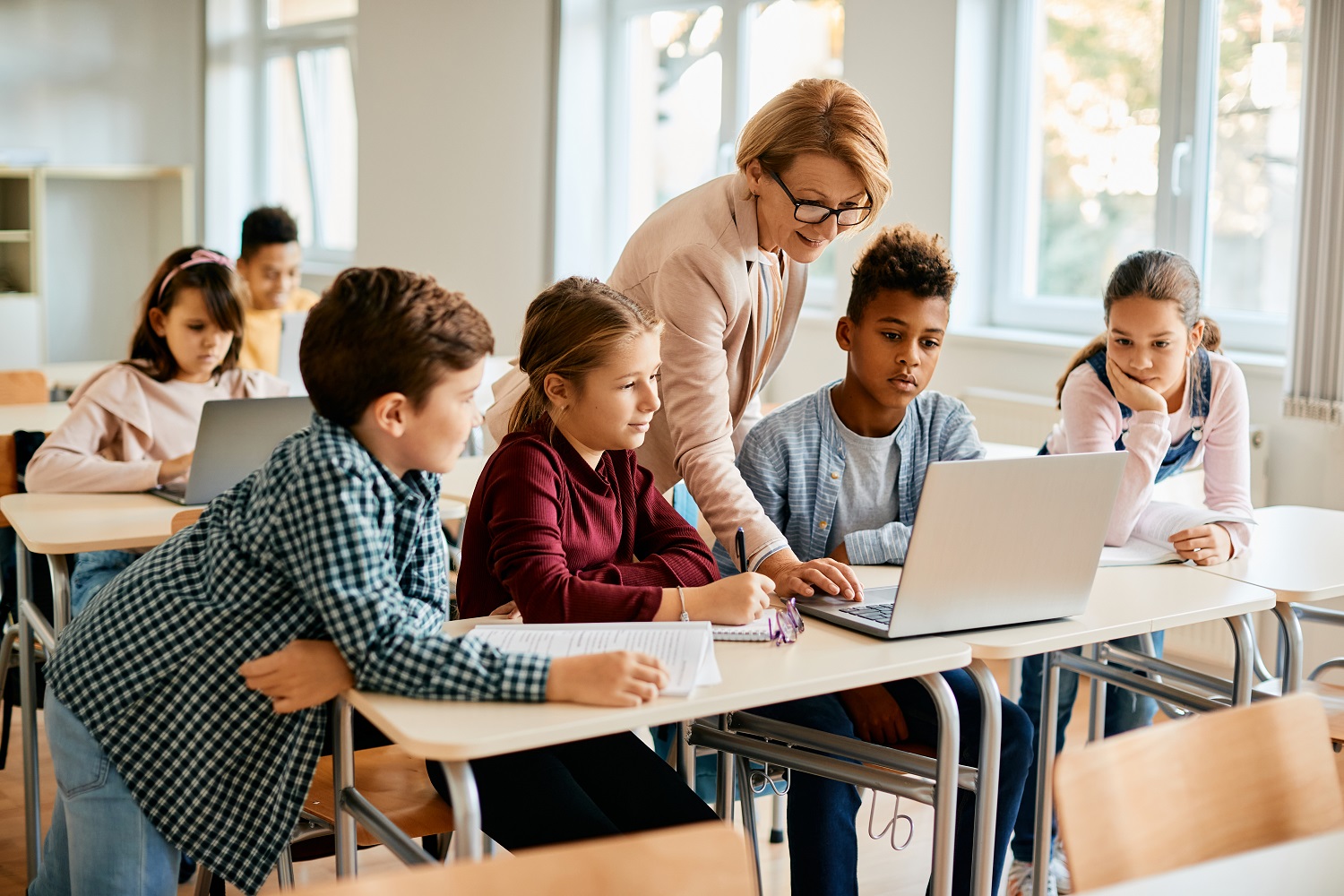 A teacher and her students using a laptop in a classroom.