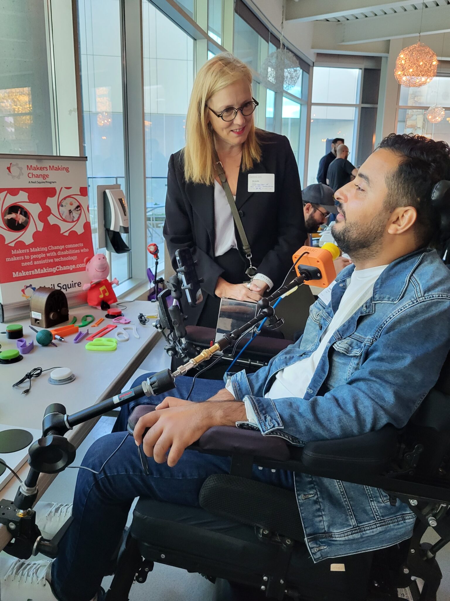 Brenda Bailey, the BC Minister of Jobs, Economic Development and Innovation talks with a gamer in a wheelchair, as he tests out the joystick.