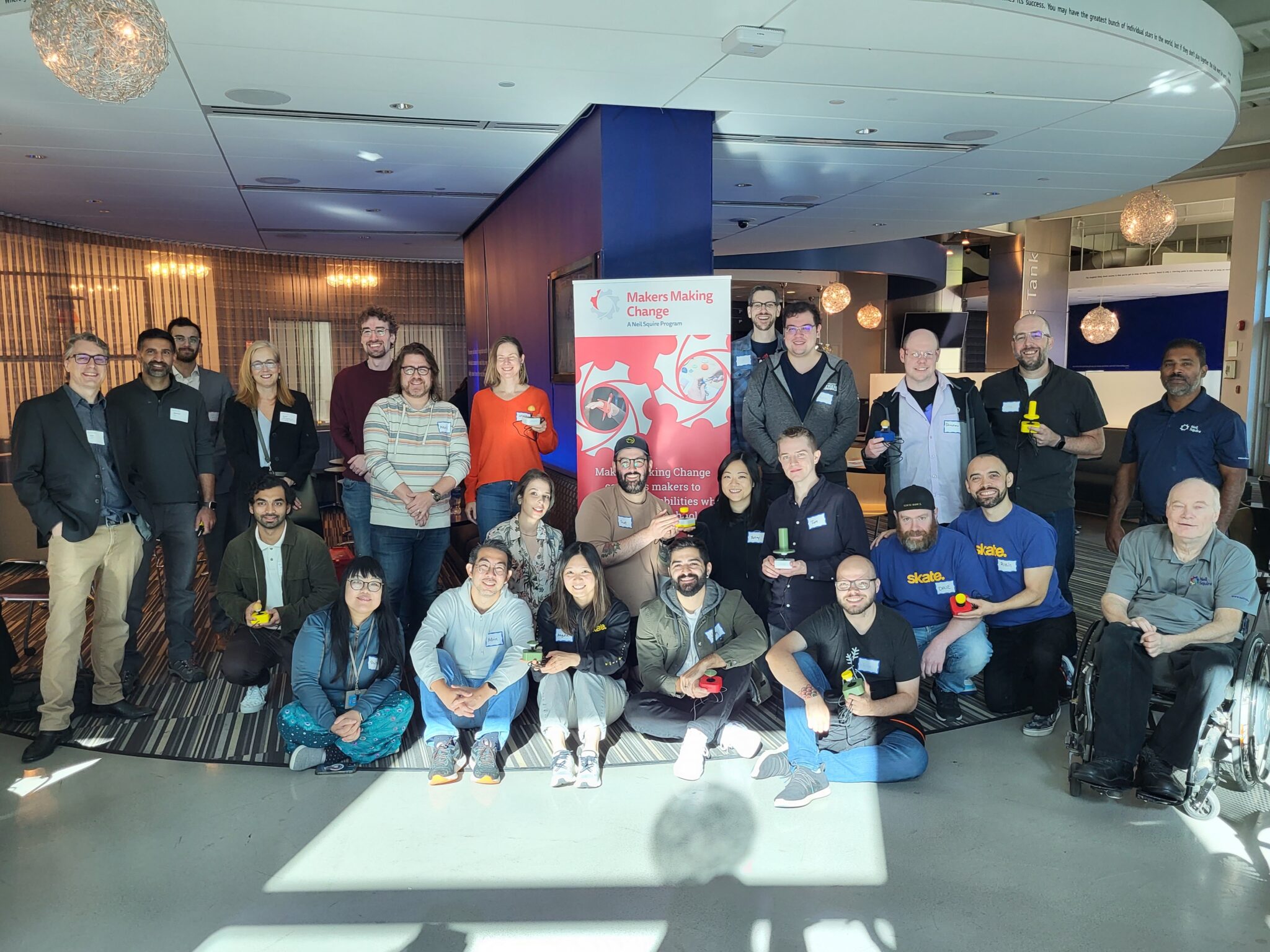 Full Circle staff showing off their adapted toys in a group photo, along with Neil Squire staff, guests, Executive Director Gary Birch, and BC Minister of Jobs, Economic Development and Innovation Brenda Bailey.