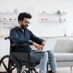 A man in a wheelchair uses a laptop.