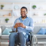 A man in a wheelchair smiles while he uses his phone.