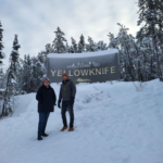 Colleen and Patrick in front of a Welcome to Yellowknife sign, standing in snow.