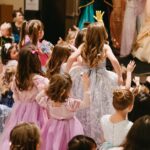 Children wearing princess dresses at the Princess Ball watching the princesses on stage.