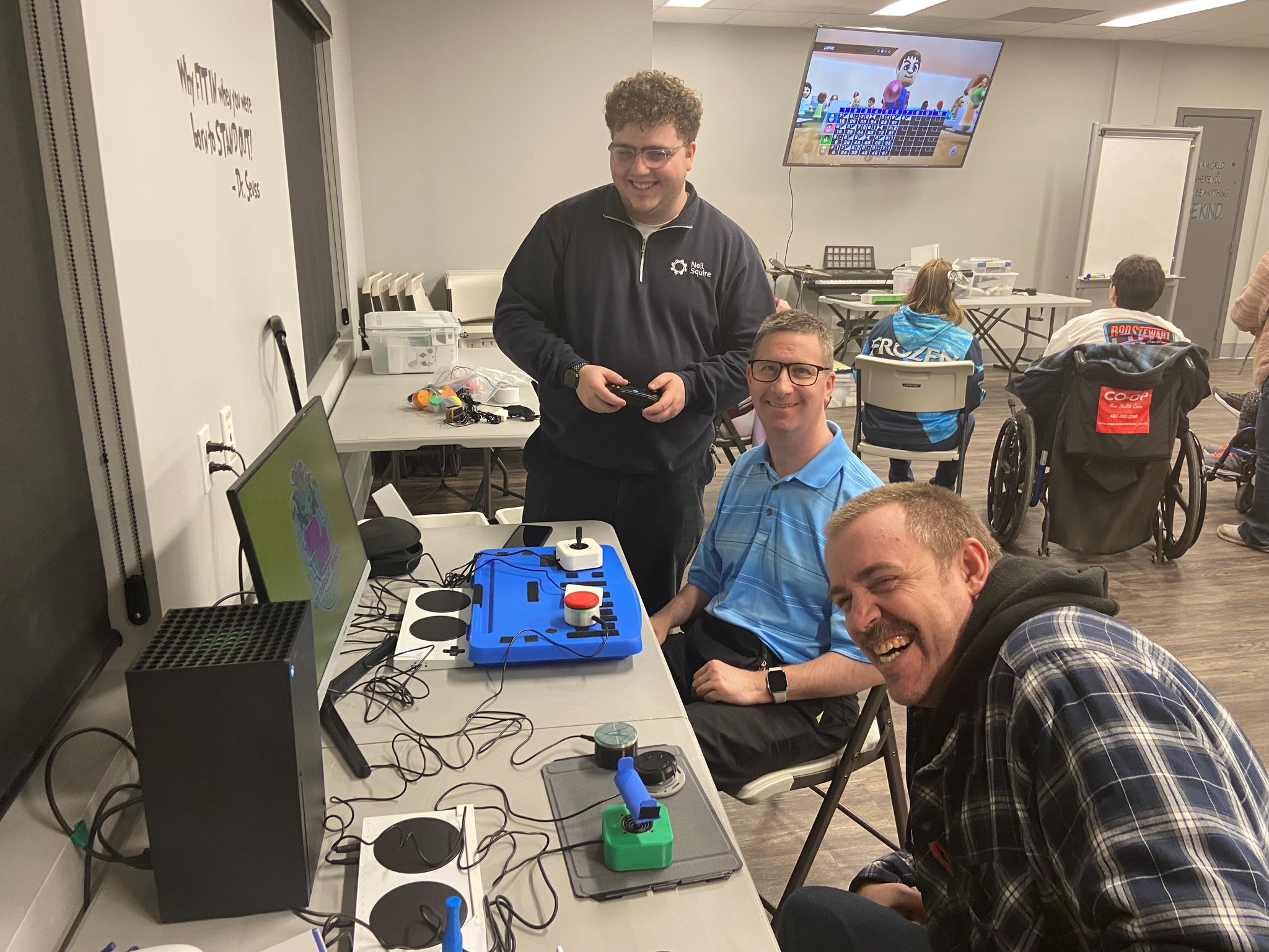 Tyler shows two Cerebral Palsy Alberta participants an adaptive gaming set-up.