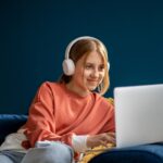 A young woman uses a laptop while wearing headphones.