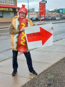 A staff member in a hot dog suit holds a sign pointing to the free hot dogs.