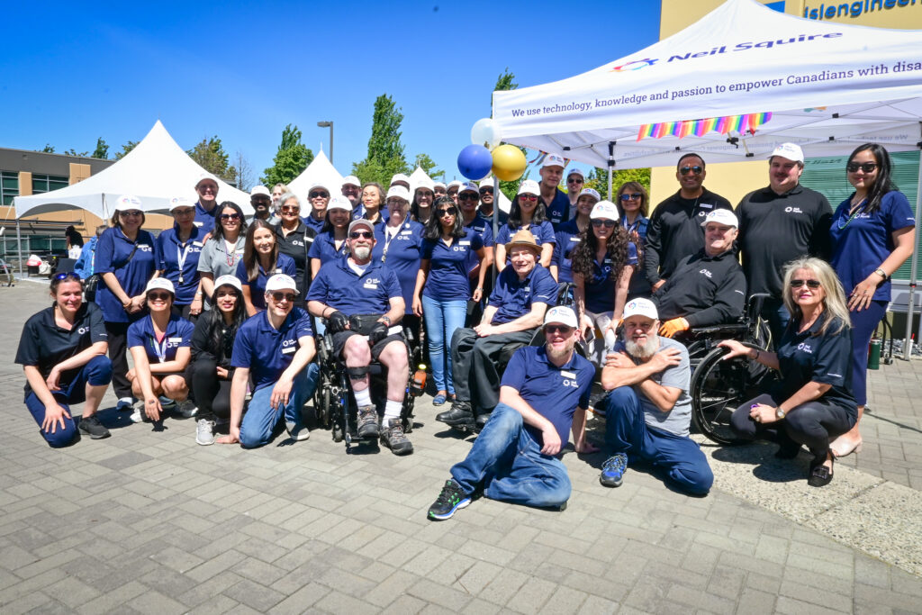 Neil Squire staff all pose together next to the Neil Squire tent outside the Burnaby office.