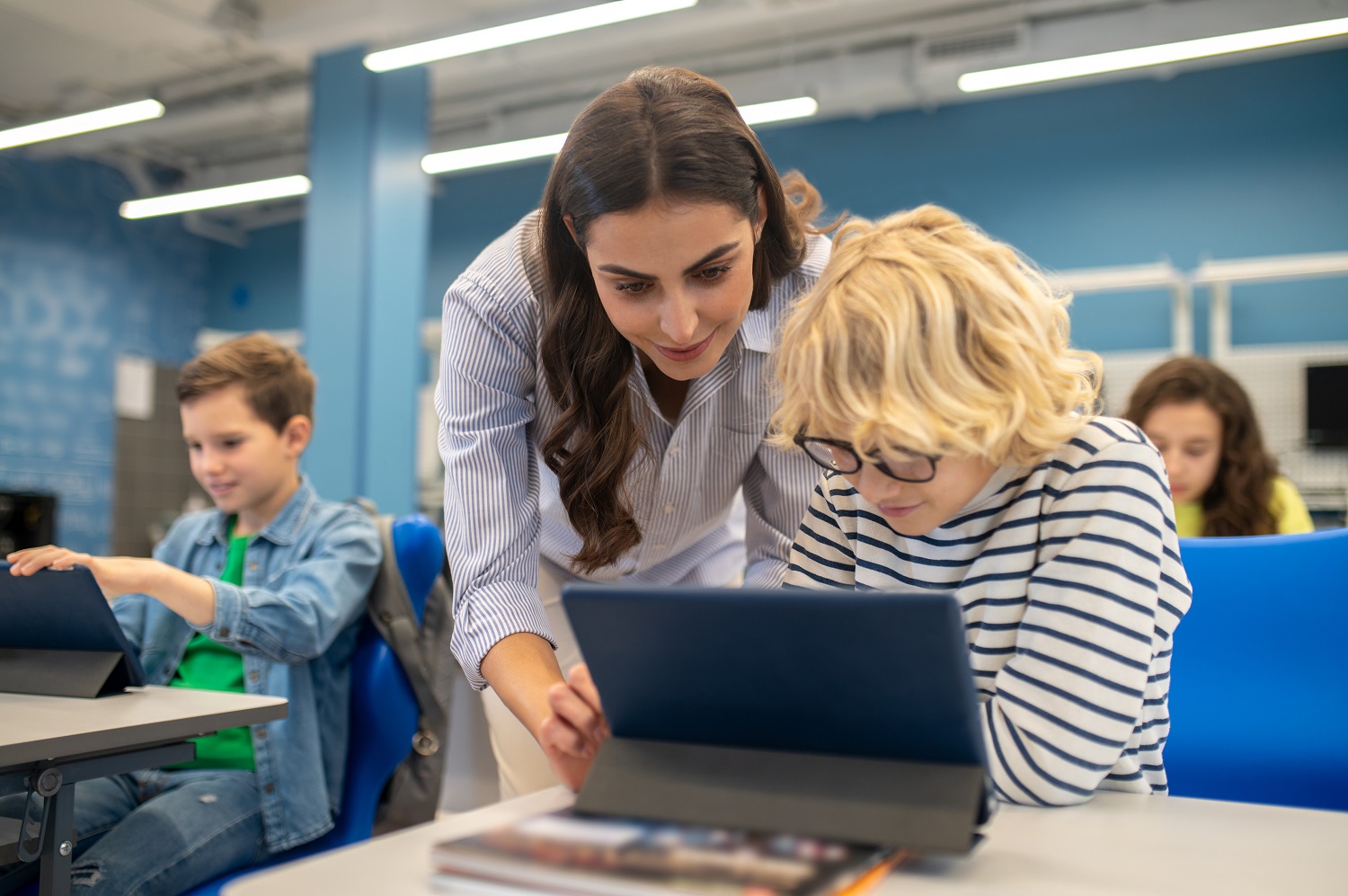 A teacher helps a student using a tablet.