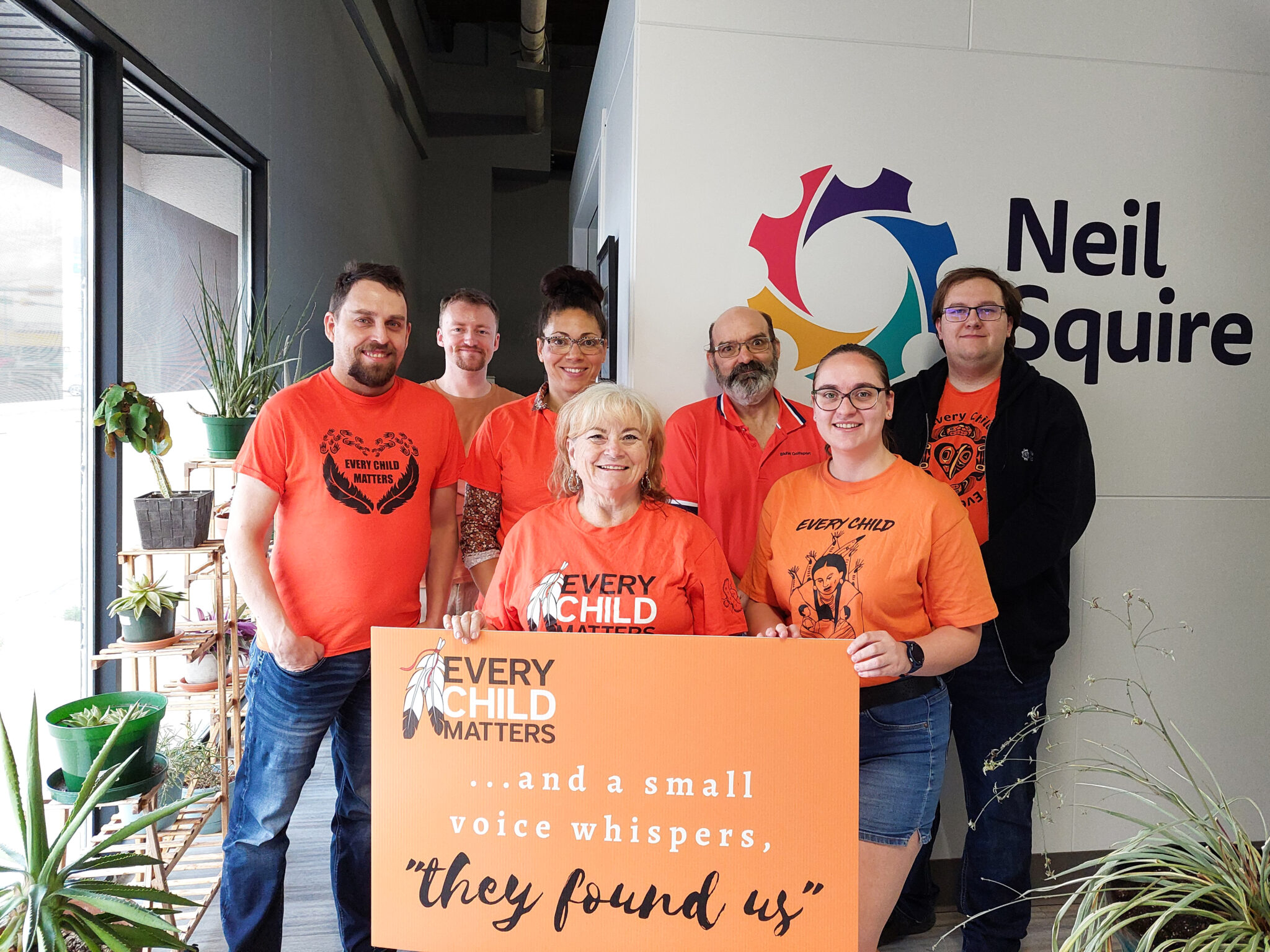 Neil Squire Regina staff wearing orange shirts and holding a banner that says, "Every child matters... and a small voice whispers, they found us"